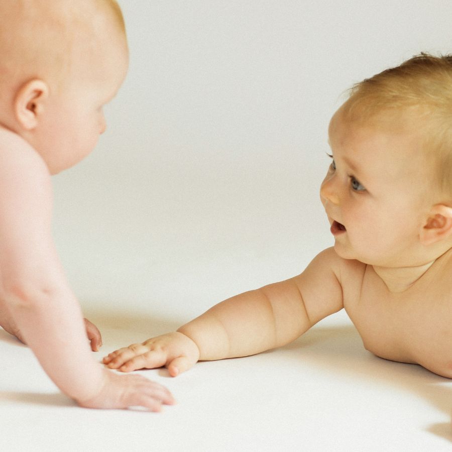 2 Babies spielen in PEKiP Kurs in der Praxis Nestwärme und schauen sich an