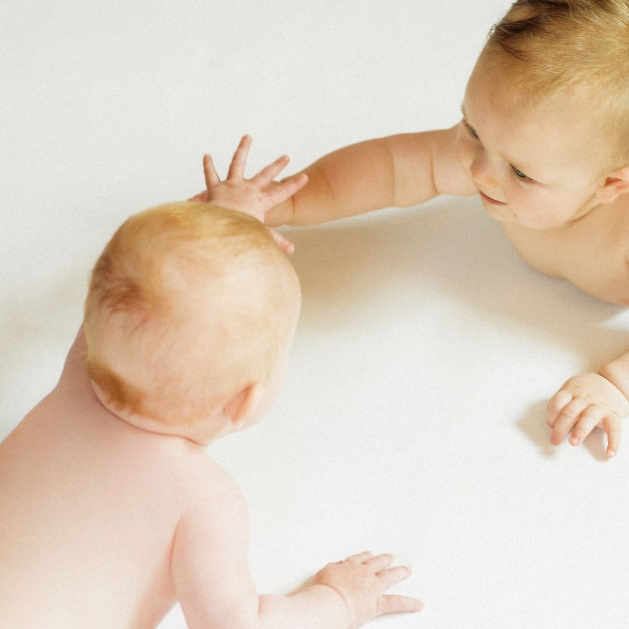 Zwei Babies spielen miteinander in der Praxis Nestwärme in München. Die Praxis Nestwärme bietet Babymassage in München an.