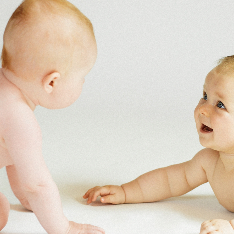2 Babies lachen sich an in einem PEKiP Kurs in der Praxis Nestwärme in München West